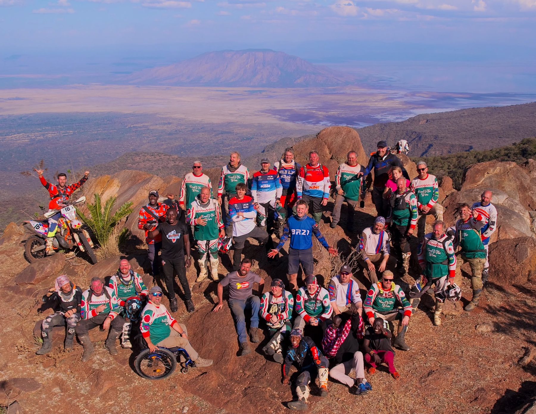 The whole team, including a rider in a wheelchair, on a rocky hilltop above the Rift Valley